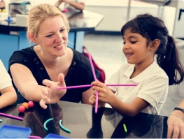 A teacher smiling and working with a young student at a classroom table